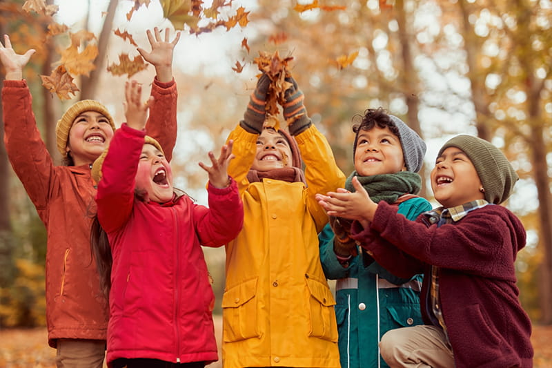 Kinder haben Spaß beim Hochwerfen von Laub im Herbstwald.